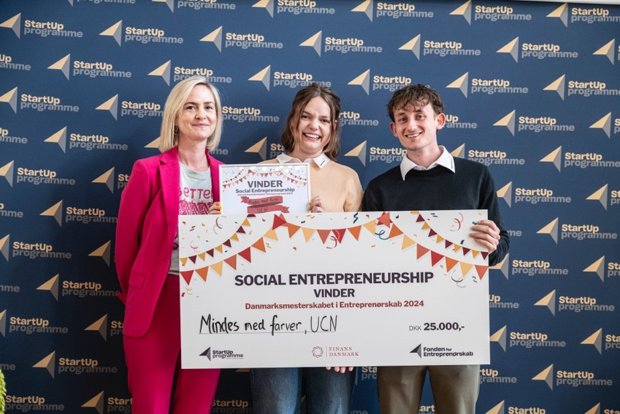 Stifterne bag virksomheden står på scenen med deres præmiecheck og bevis fra danmarksmesterskaberne i social entreprenørskab