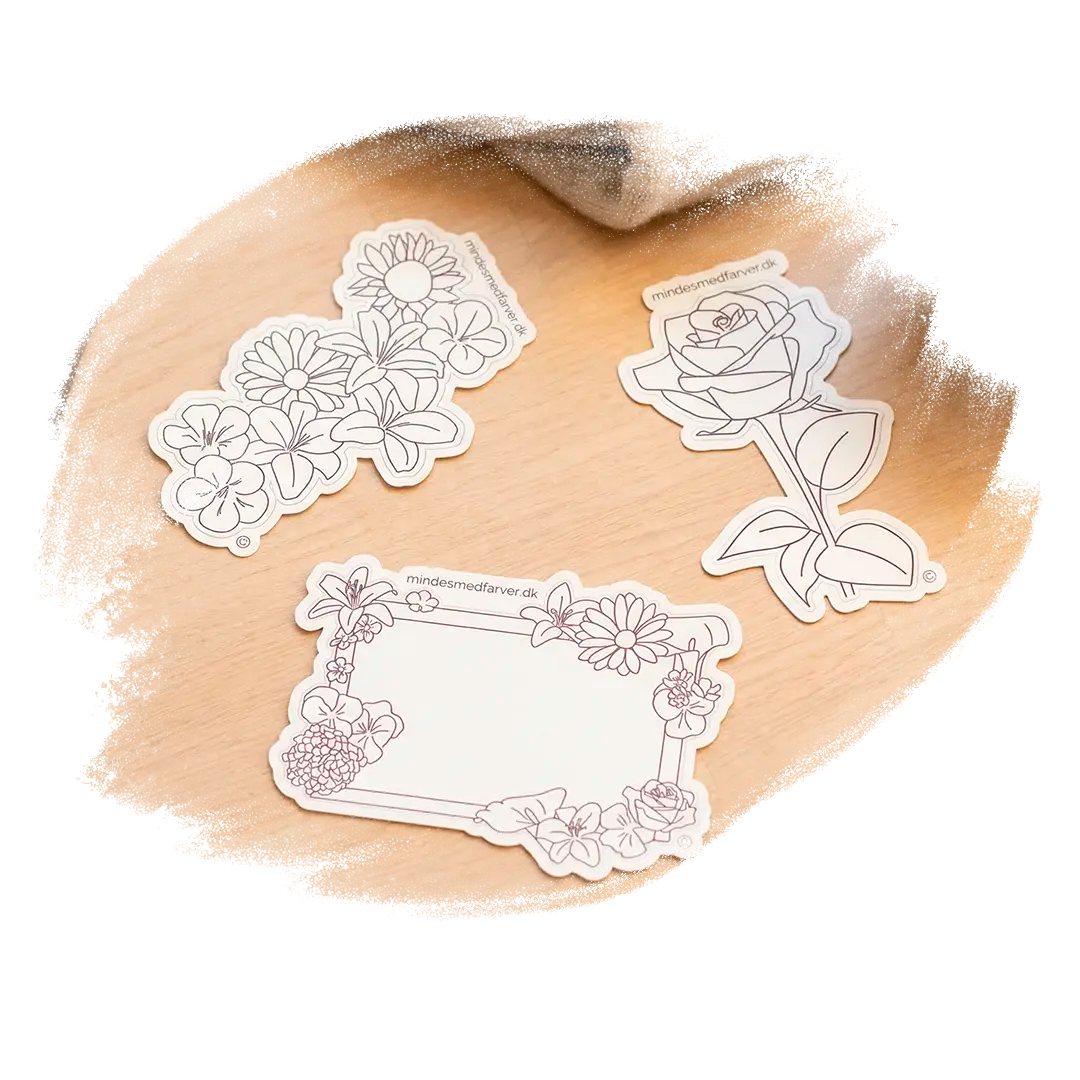 Tre store klistermærker som ligger på et bord. Viser en rose, en buket og en ramme.