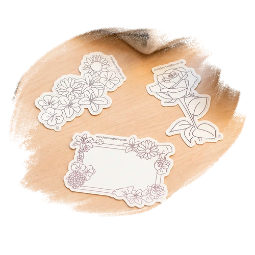 Tre store klistermærker som ligger på et bord. Viser en rose, en buket og en ramme.